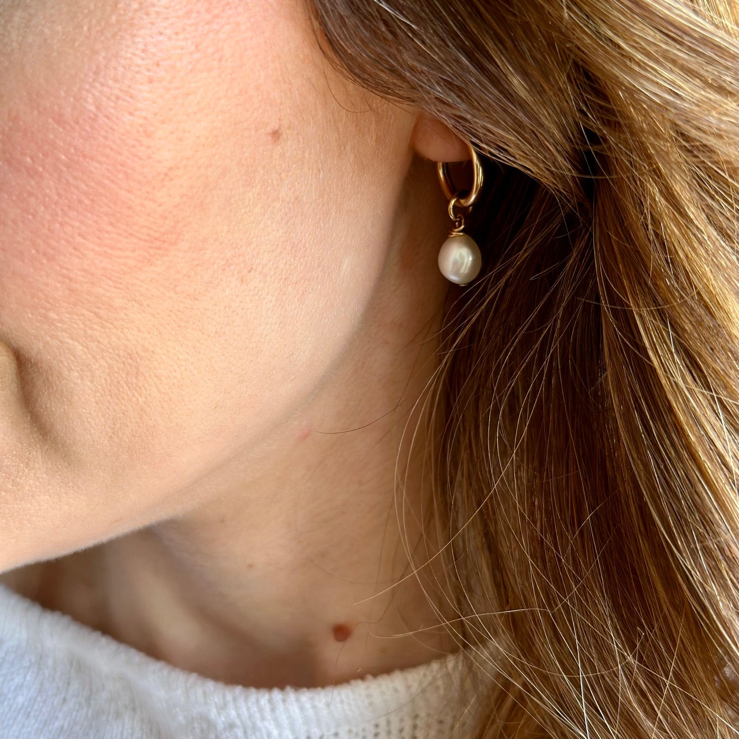 Close-up of a person wearing a gold earring with a pearl drop.